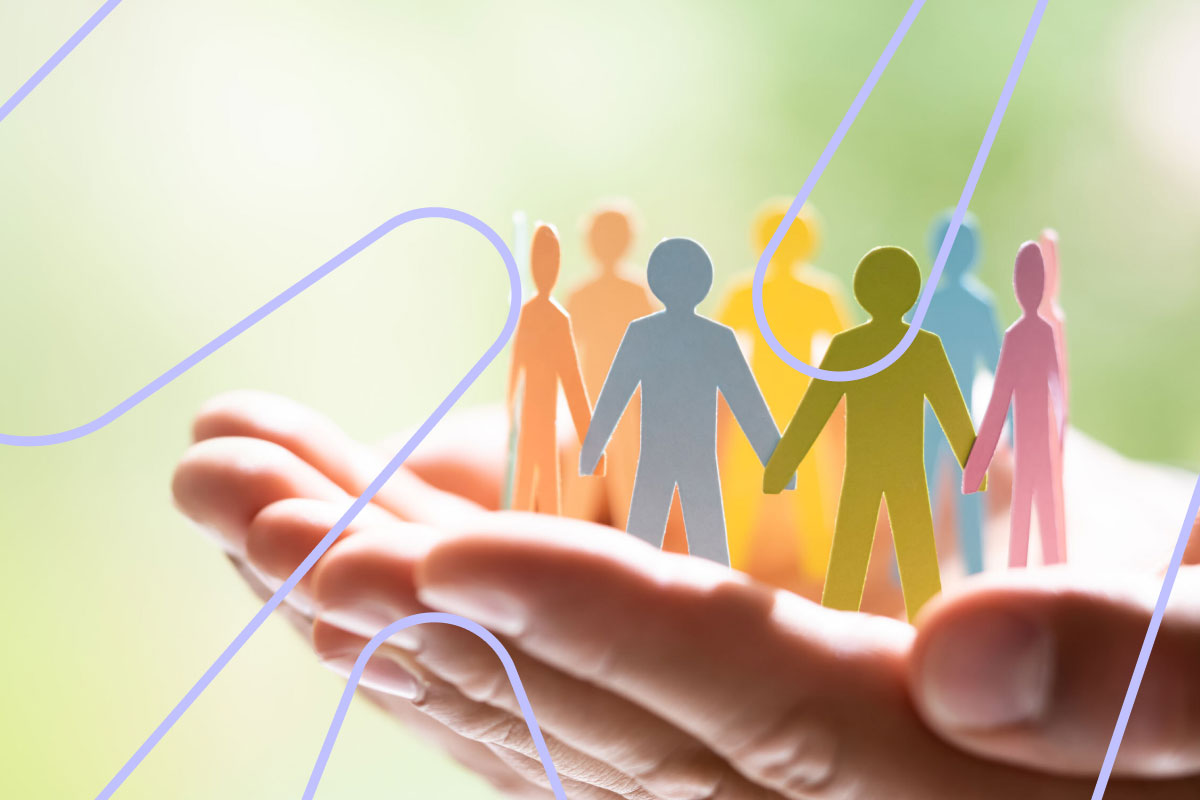 En menneskehånd holder flere små papir figurer som holder hender i ring.